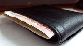 zugeklappte schwarze Geldbörsel, aus der ein Geldschein rausschaut.