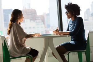 Zwei Frauen unterschiedlicher Hautfarbe sitzten sich an einem Tisch gegenüber und unterhalten sich. 