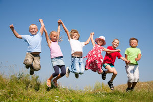 6 lachende Kinder halten sich an den Händen und springen dabei in die Luft.