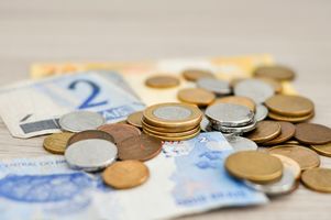 viele verschiedene Geldscheine und Münzen liegen durcheinander verteilt auf einem Tisch.