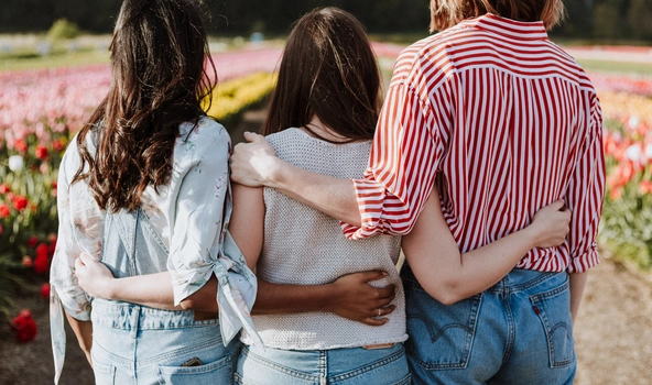 Drei Frauen stehen Arm in Arm vor einem Blumenfeld.