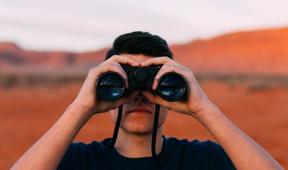 Ein Mann steht in einer Wüste und schaut durch ein Fernglas.