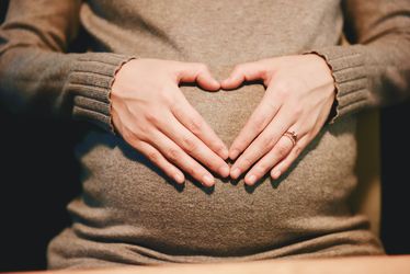 Bauch einer schwangeren Frau. Sie hat ihre Hände auf den Bauch gelegt, sodass die Form eines Herzes entsteht.