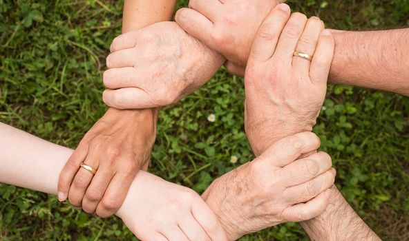 6 Hände umfassen alle die Handgelenke der rechten Nebenperson. Aus den Händen entsteht damit ein Kreis.