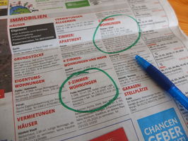 aufgeschlagener Immobilienteil einer Zeitung. Mehrere Anzeigen sind mit grünem Filzstift markiert. Ein Kugelschreiber liegt auf der Zeitung. 