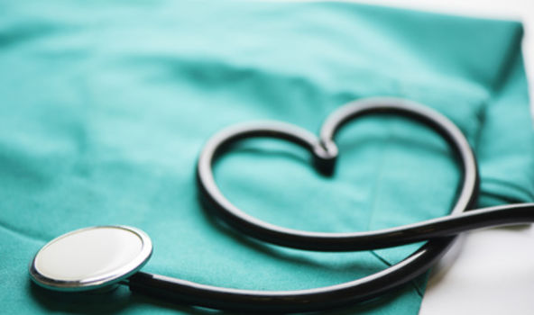 Stethoskop liegt auf grüner Klinik-Bekleidung. Der Schlauch ist als Herz geformt.
