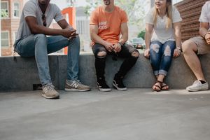 Vier Personen mit lockerem Outfit sitzen auf einer Steinbank.