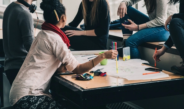 5 Personen sitzen um einen Tisch herum und unterhlaten sich.