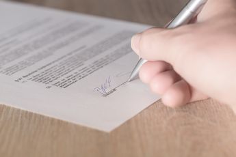 Gedruckter Vertrag, der gerade von jemandem mit einem Kugelschreiber unterschrieben wird. 