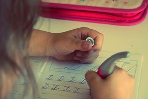 Ein Kind übt in einem Schreiheft Schreibschrift. Es schreibt gerade den Buchstaben "L" mehrmals in die Zeilen des Hefts.