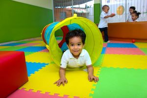 Ein kleines Kind krabbelt durch einen Kriechtunnel heraus. Im Hintergrund spielen 3 weitere Kinder zusammen.