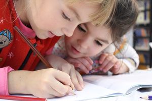 Zwei kleine Kinder beugen sich interessiert über ein Heft. Eines der Kinder schreibt etwas in das Heft hinein.