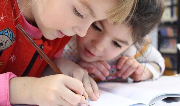 Zwei kleine Kinder beugen sich interessiert über ein Heft. Eines der Kinder schreibt etwas in das Heft hinein.