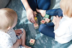 Zwei kleine Kinder spielen mit Bauklötzen. Man sieht auch die Hand einer Betreuerin.